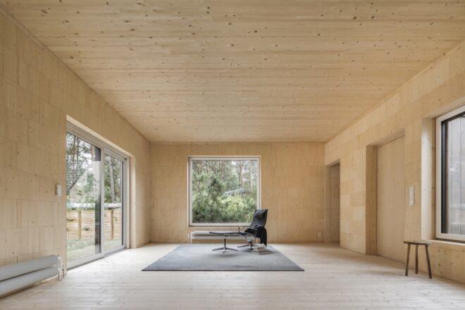 dark chair and table and gray rug in a light wood-lined room with large square openings