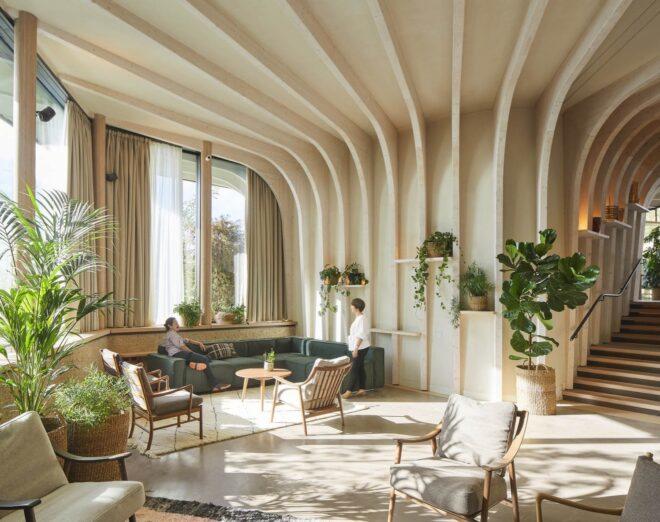 green sofa and beige chairs in a room with curving wood walls covered in plants