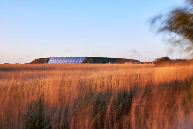 large hill with a white ETFE structure built into the center surrounded by tall grasses