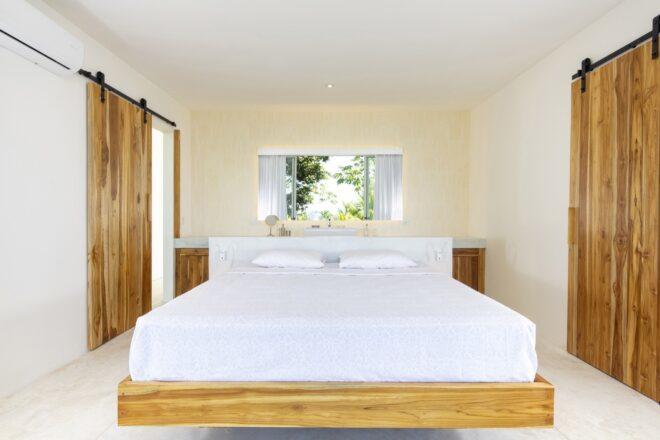 a bedroom with a white bed on a wood frame and a window above the bed