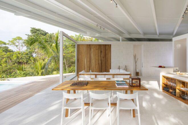 an indoor-outdoor dining area with a wood table and white chairs