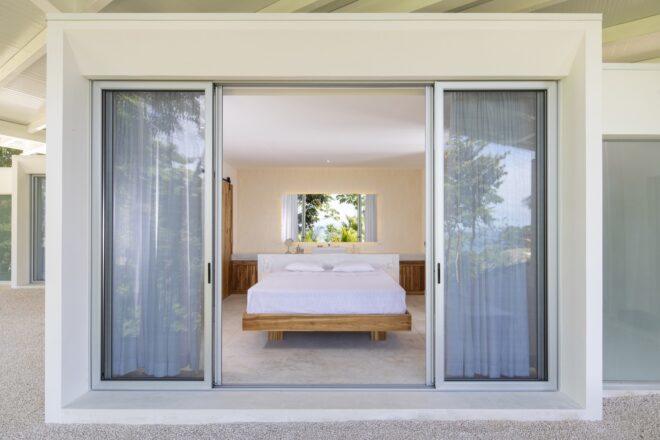sliding glass doors with blue curtains that open up to a bedroom with a white bed on a wood frame