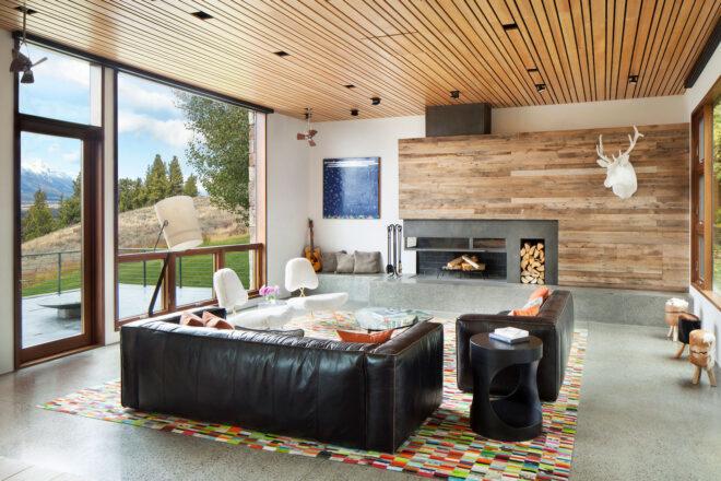living room with wood ceilings and walls and two black leather sofas facing a fireplace