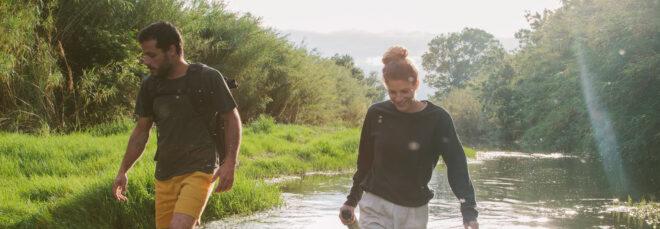 two people wearing hemp shirts and shorts while walking in a creek