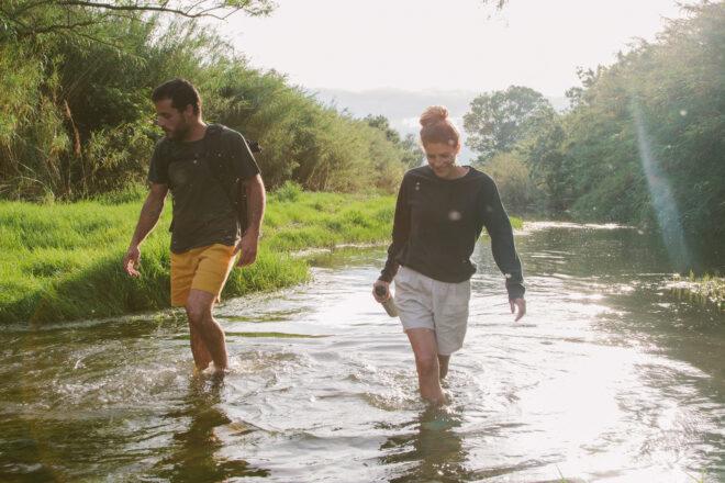 two people wearing hemp shirts and shorts while walking in a creek