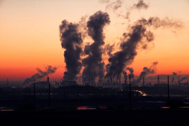 smoke emerging from a factory against a dark sunset background