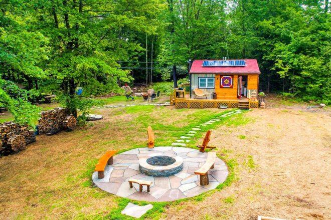 solar panels on top of a wood and metal tiny home near a fire pit
