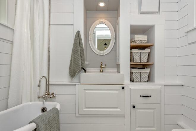 a white bathroom with a small mirror above the sink