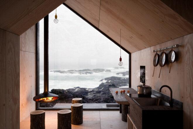 small cabin interior with one large wall of glass revealing mountain views