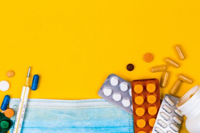 paper mask, thermometer and bottles of medicine on yellow background