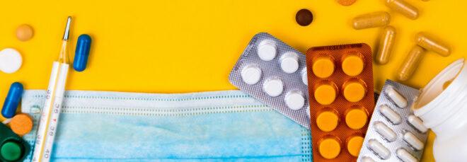paper mask, thermometer and bottles of medicine on yellow background