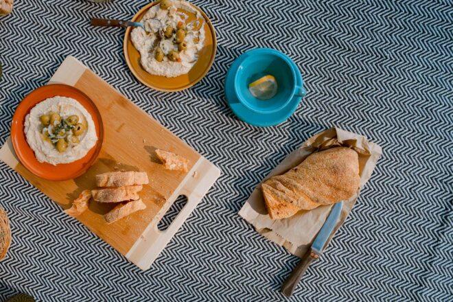bowls of hummus, plate of bread and a wood cutting board on a blue and white blanket