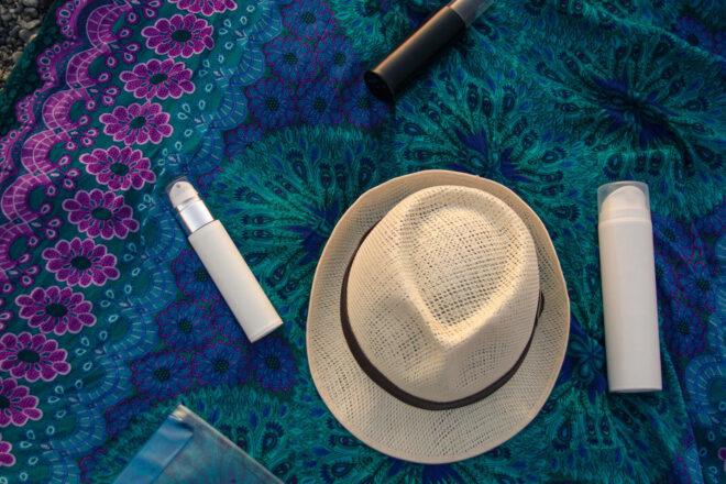 straw hat and three bottles of sunscreen and lotion on a purple and blue blanket
