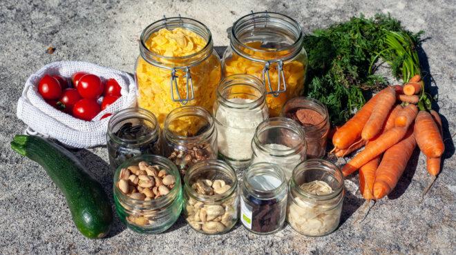 glass jars of nuts and pasta next to carrots, zucchini and tomatoes in a reusable produce bag