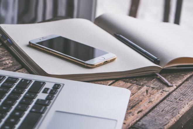 close-up of laptop beside a phone and a notebook