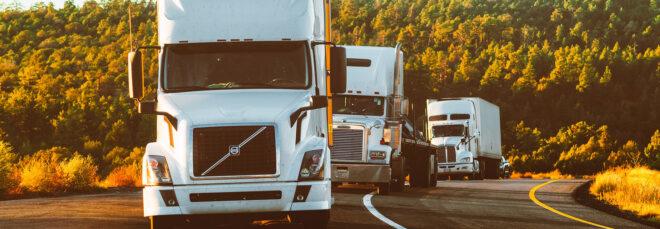 a line of three trucks on a road with trees in the background