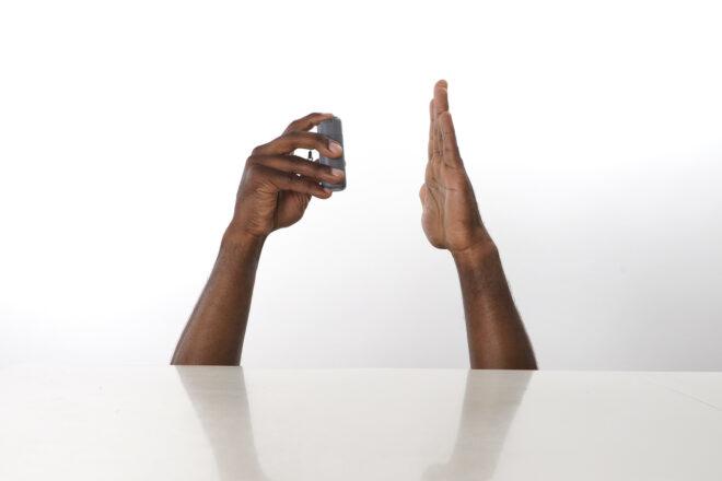 to the left, a hand holding a gray bottle of sanitizer spraying into an open hand on the right