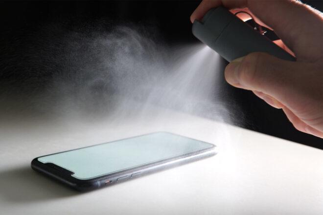 on the right, a hand sprays sanitizer on a phone to the left
