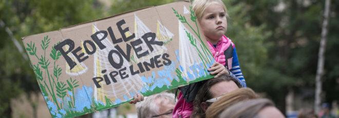 a child on someone's shoulders, holding a sign that says "people over pipelines."