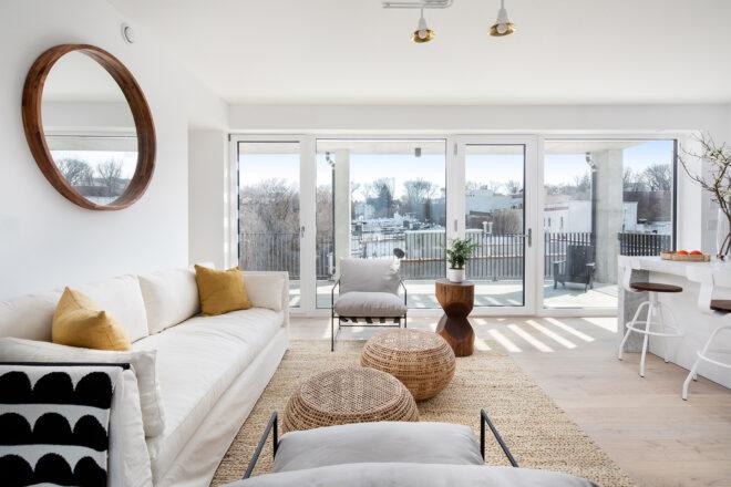 white sofa and wicker tables beside wall of sliding glass doors revealing view of NYC