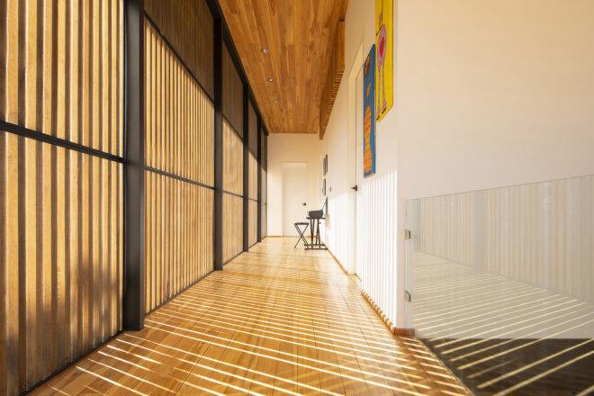 a hallway with wood floors and white walls. to the left is a wood lattice wall that lets in beams of sunlight.