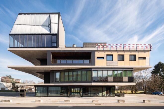 large glass and concrete building topped with a white extension