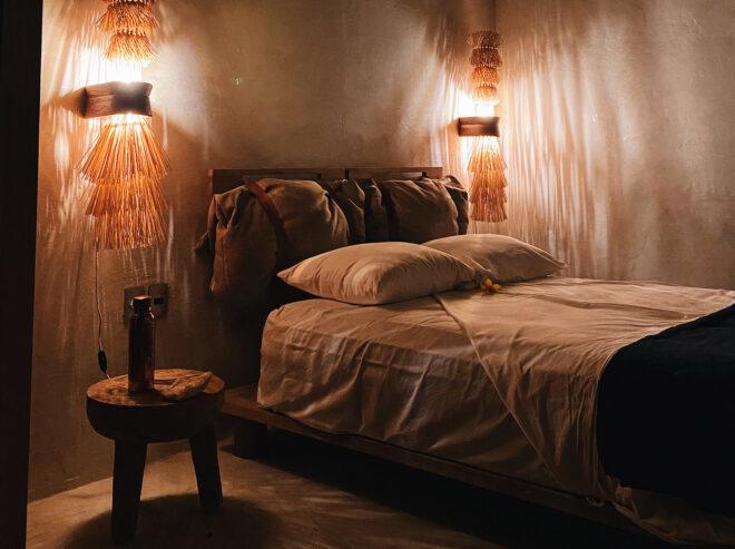 a bedroom with white sheets and a round bedside table. on either side of the bed are three tier fringed wall fixture lights.