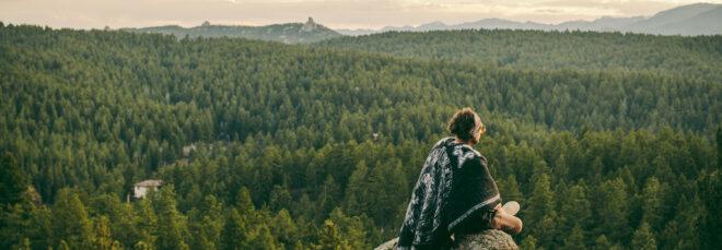 person sitting on rock looking out toward a forest