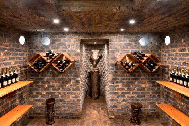 a brick cellar with diamond-shaped wood wine shelves full of wine bottles. in the middle of the room is an in-set area with what appears to be a cow skull on the wall.