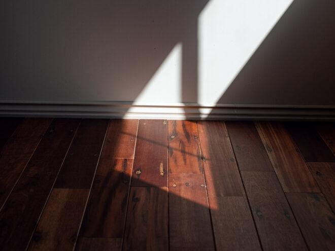 bright light and shadows against a white wall and dark wood floors