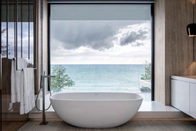 freestanding soaking tub beside glass wall revealing views of a lake