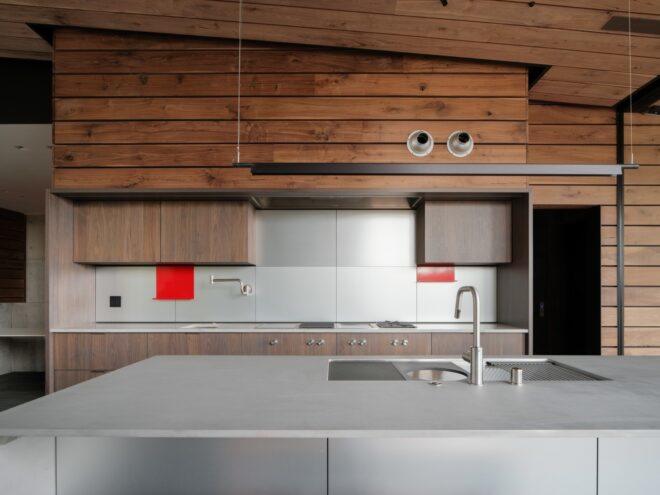 a kitchen with a gray island with sink. in the background are white-topped wood counters and cabinetry, with two red accents on the wall.