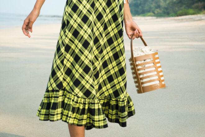 person in yellow and black plaid dress carrying brown vegan leather bucket purse
