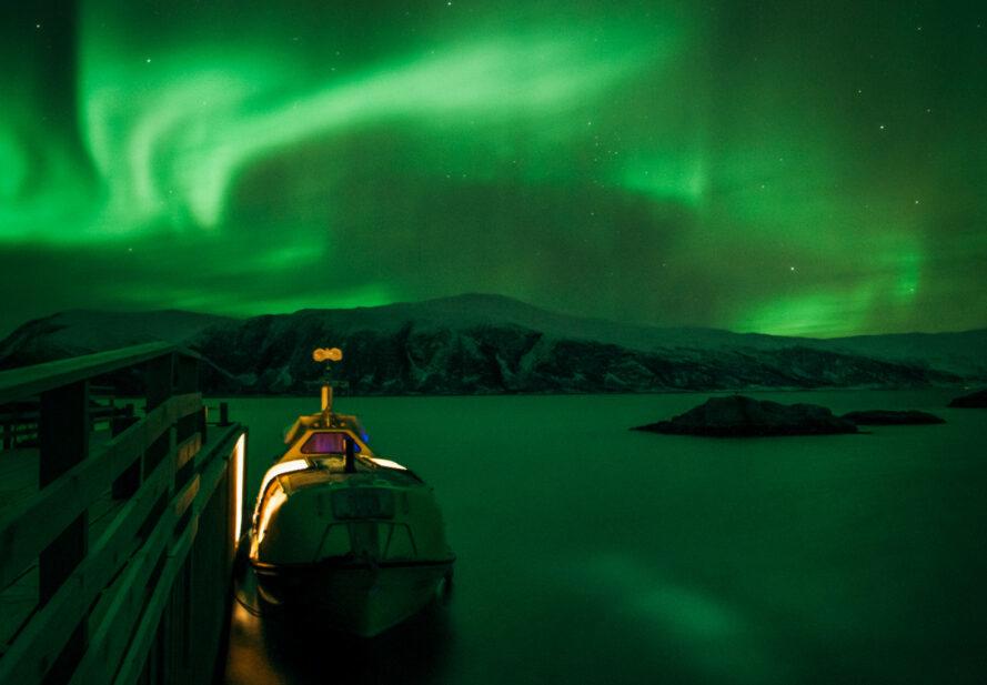 boat docked and facing sky filled with green Northern Lights display