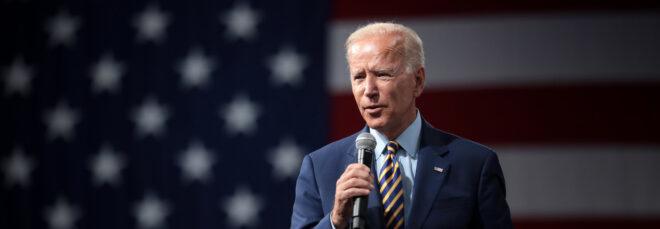 Joe Biden speaking into a microphone with American Flag in the background