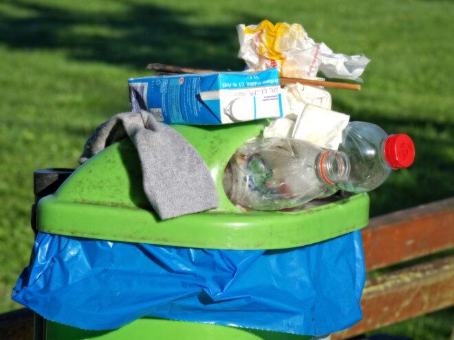 green recycling bin overflowing with plastic and cardboard containers