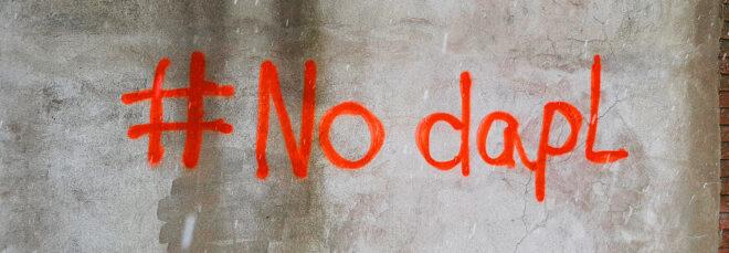 red-orange graffiti reading "#No dapl" against a grey wall