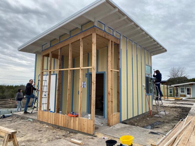 three people surround a house being built