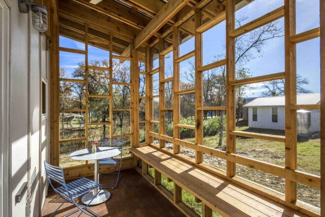 a sitting area inside a home with walls made of wood and glass. inside, there is a small round table with two chairs.