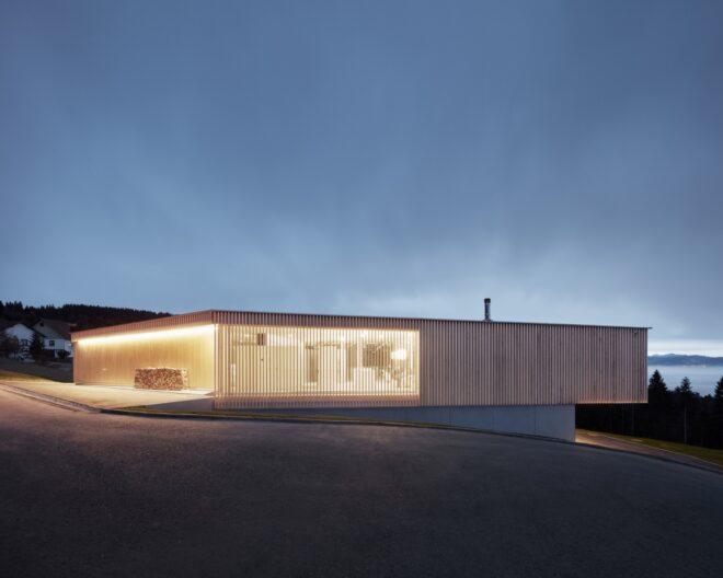 a streetview of the home's second story. vertical timber slats make up the facade, through which bright indoor lighting filters through.