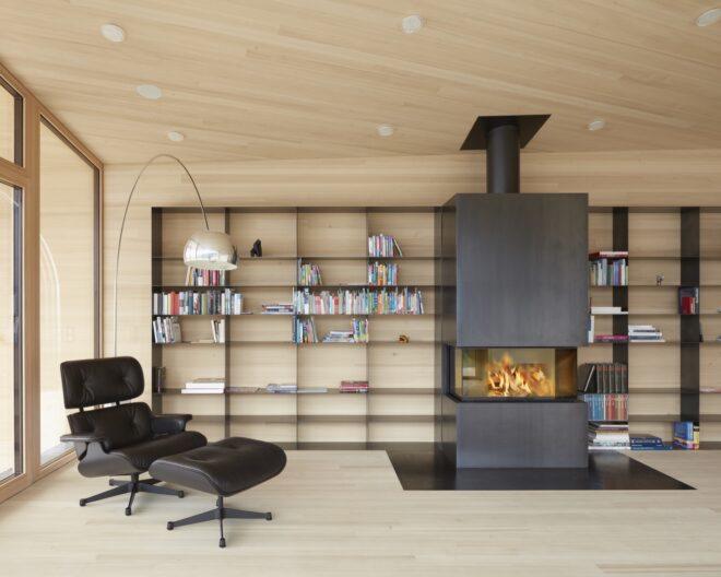a living space where a floor lamp hangs over a dark leather-look chair and foot stool. behind the chair, a black bookshelf stands against the wall next to a fireplace.