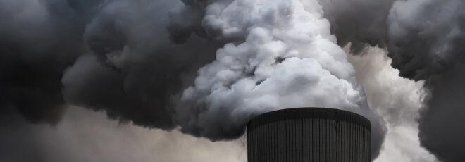 black and white image of a power plant emitting smoke into the air
