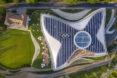an overhead view of the campus, showing abundant greenery on both the lawn and part of the roof. to the right, the building itself features a butterfly-shaped solar display on the roof, with the olympic logo on it.