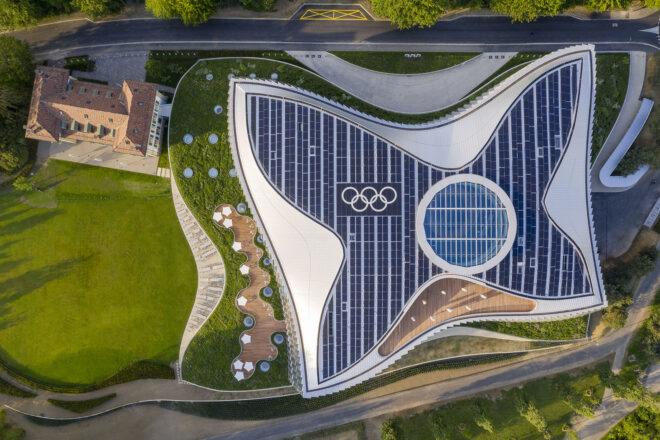 an overhead view of the campus, showing abundant greenery on both the lawn and part of the roof. to the right, the building itself features a butterfly-shaped solar display on the roof, with the olympic logo on it.