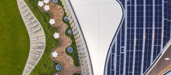 an overhead view of the campus, showing abundant greenery on both the lawn and part of the roof. to the right, a white wavy design contracts with solar panels on the roof.