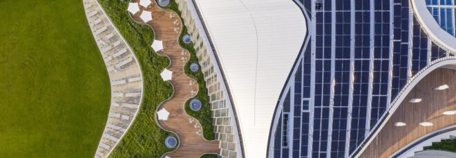 an overhead view of the campus, showing abundant greenery on both the lawn and part of the roof. to the right, a white wavy design contracts with solar panels on the roof.