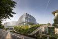 a wavy building with a sectioned glass facade. sloping rooftops incorporate greenery into the design.