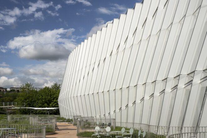 the side of the building, showing a white facade. below, a small patio incorporates green spaces among chairs and tables.