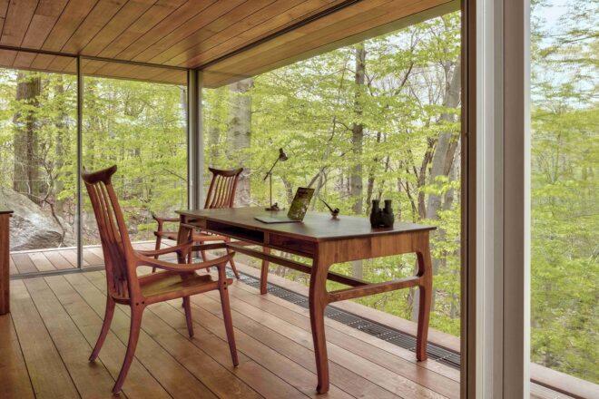 wood chair at wood desk in room with glass walls revealing forest views