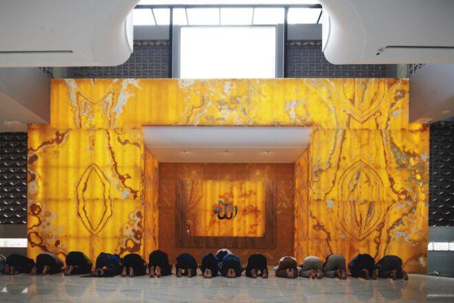 people kneeling in front of yellow prayer space in a mosque